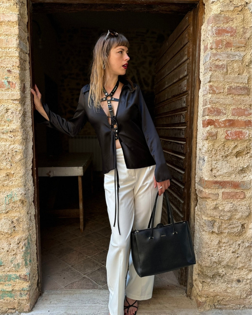 BlackTulip Leder Accessoire in Schwarz  - veredelt mit grünem Strass, auf der Haut unter einer schwarzen Satinbluse, dazu eine weiße Hose und eine schwarze Handtasche. Und natürlich Highheels. Eleganter Stil. Hier blitzt der obere Teil des  BlackTulips mit seinem grünen Strass  auf. Ganzkörperaufnahme  - XMORENIUM-NERO