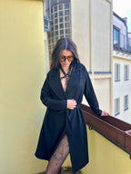 BlackTulip Leder Accessoire in Schwarz  - veredelt mit grünem Strass, auf der Haut unter einem schwarzen Mantel. 
Eleganter Stil. Hier blitzt der obere Teil des  BlackTulips mit seinem grünen Strass  auf. Ganzkörperaufnahme  - XMORENIUM-NERO