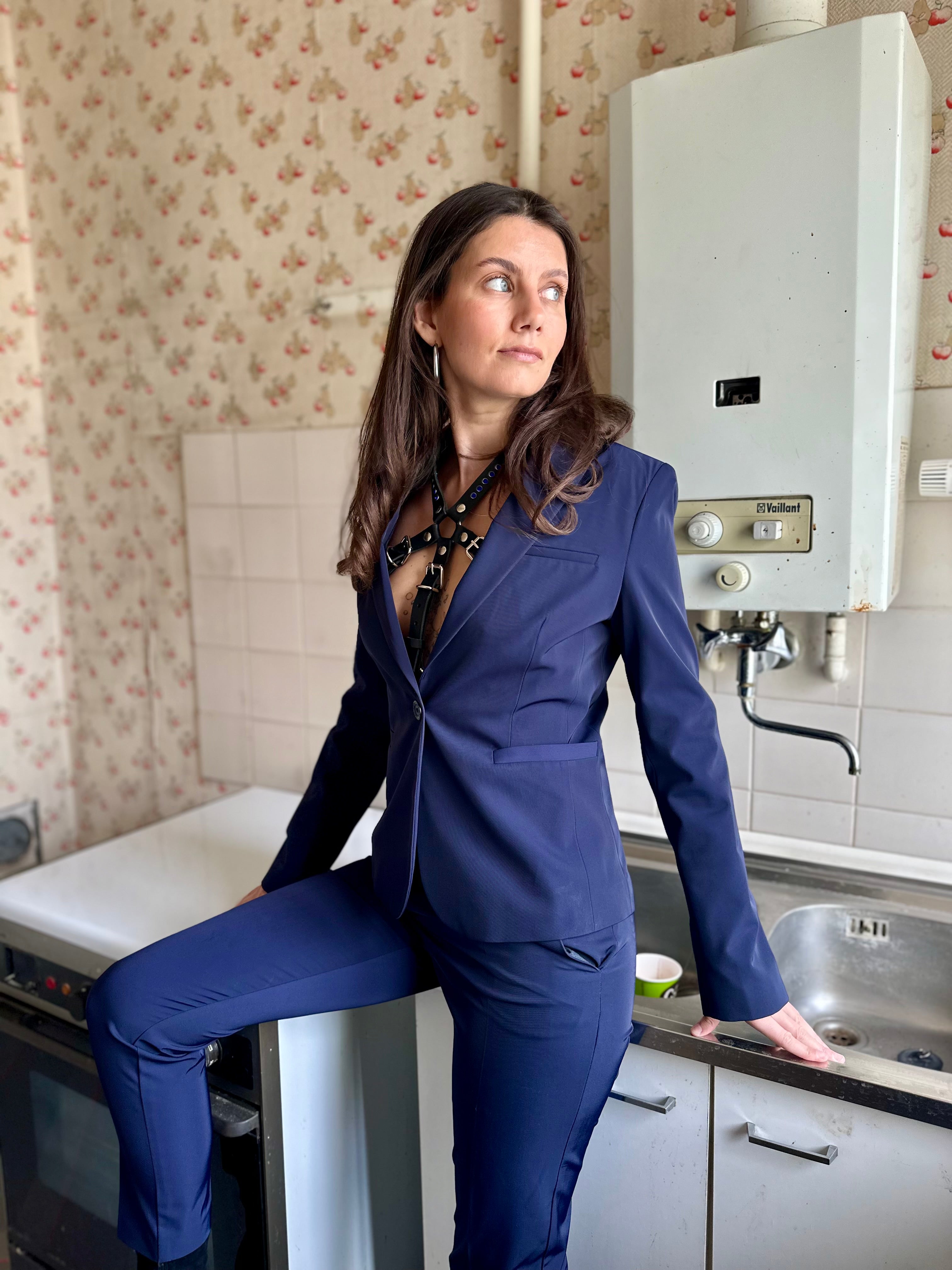 BlackTulip Leder Accessoire mit blauem Strass veredelt, getragen unter dem Jackett eines Hosenanzugs, Ganzkörperaufnahme - XMORENIUM-NERO