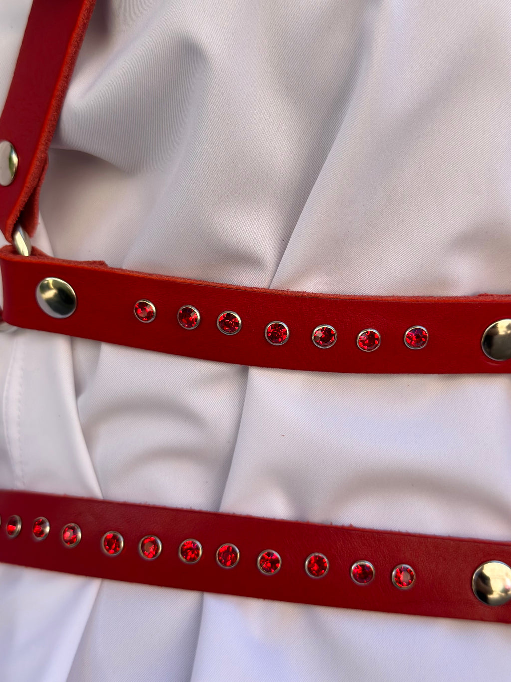 RedTulip Leder Accessoire in Rot mit Rotem Strass veredelt, auf weißer Bluse getragen. Hier blitzen die 2 unteren Leder Riemen des  RedTulip RedDiamant mit seinem rotem Strass auf. Detailaufnahme - XMORENIUM-NERO