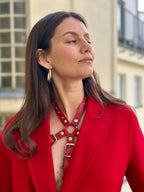 RedTulip Leder Accessoire in Rot mit Rotem Strass veredelt, auf der Haut unter einem roten Mantel. Hier blitzt der obere Teil des  RedTulip RedDiamant mit seinem Strass auf. Nahaufnahme - XMORENIUM-NERO