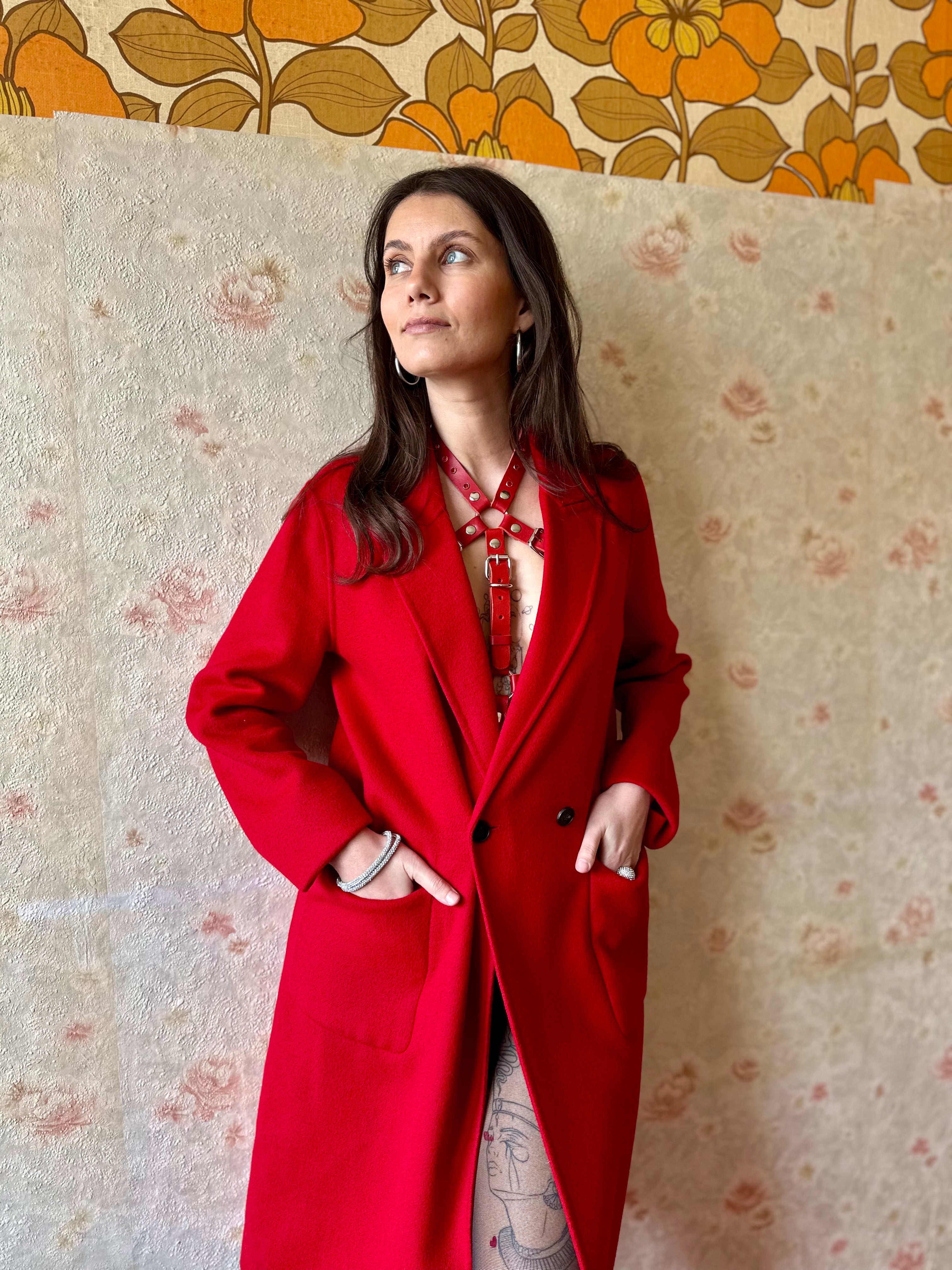 RedTulip Leder Accessoire in Rot mit Rotem Strass veredelt, auf der Haut unter einem roten Mantel. Hier blitzt der obere Teil des  RedTulip RedDiamant mit seinem Strass auf. Ganzkörperaufnahme - XMORENIUM-NERO