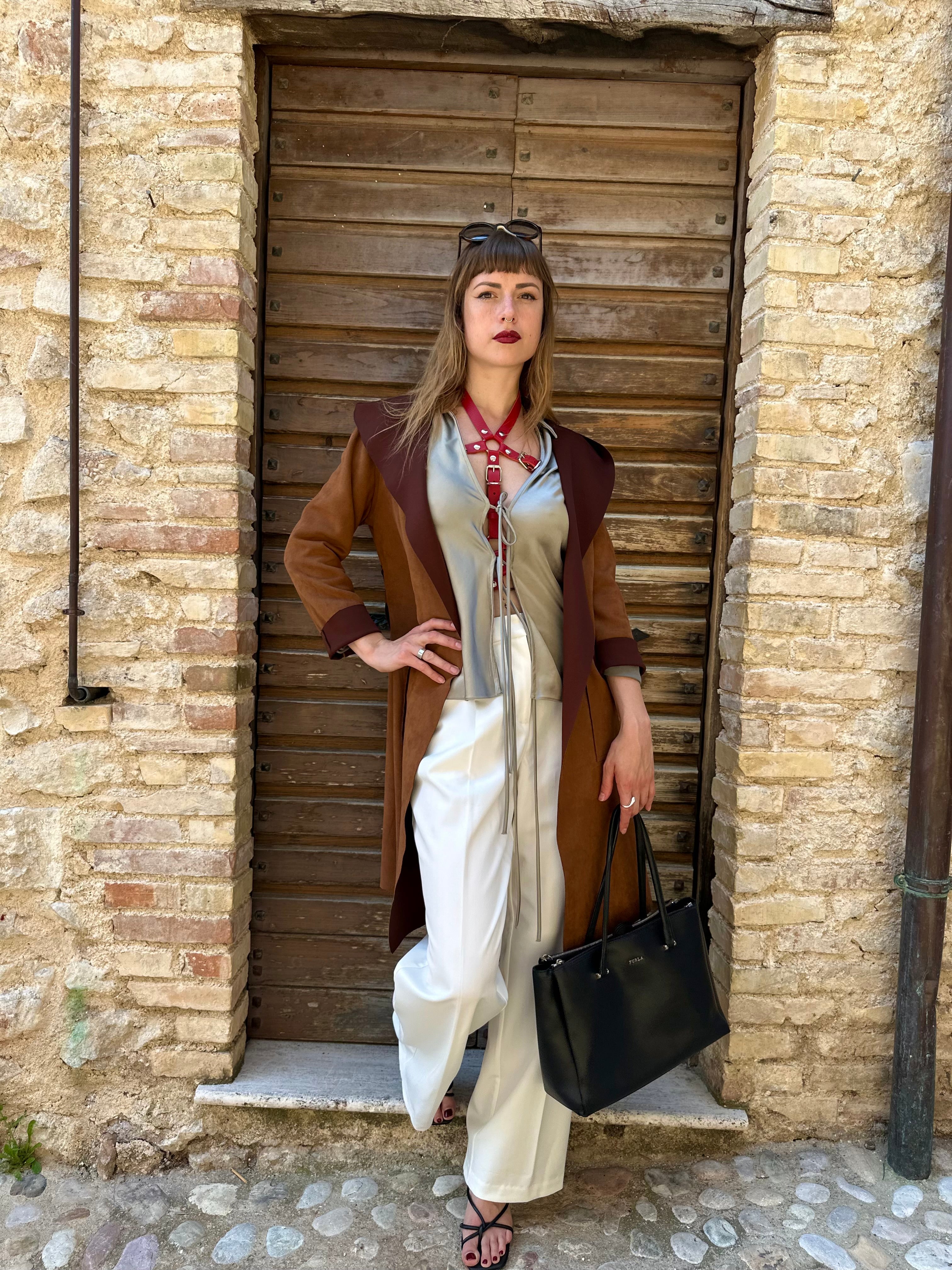 RedTulip Leder Accessoire in Rot  - das Basis Modell, auf der Haut unter einer beigen Satinbluse, dazu eine weiße Hose, einen leichten braunen Sommermantel darüber und eine schwarze Handtasche. Und natürlich Highheels. Eleganter Stil. Hier blitzt der obere Teil des  RedTulip  auf. Ganzkörperaufnahme  - XMORENIUM-NERO