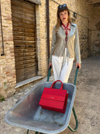 RedTulip Leder Accessoire in Rot  - das Basis Modell, auf der Haut unter einer beigen Satinbluse, dazu eine weiße Hose und eine rote Handtasche. Eleganter Stil. Hier blitzt der obere Teil des  RedTulip  auf. Ganzkörperaufnahme  -  XMORENIUM-NERO