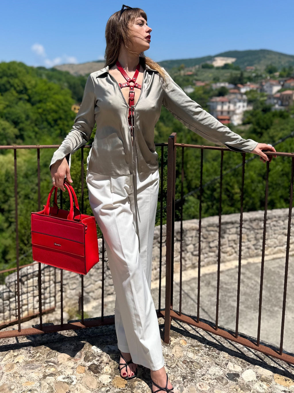 RedTulip Leder Accessoire in Rot  - das Basis Modell, auf der Haut unter einer beigen Satinbluse, dazu eine weiße Hose und eine rote Handtasche. Natürlich mit Absatzschuhen. Eleganter Stil. Hier blitzt der obere Teil des  RedTulip  auf. Ganzkörperaufnahme  - XMORENIUM-NERO