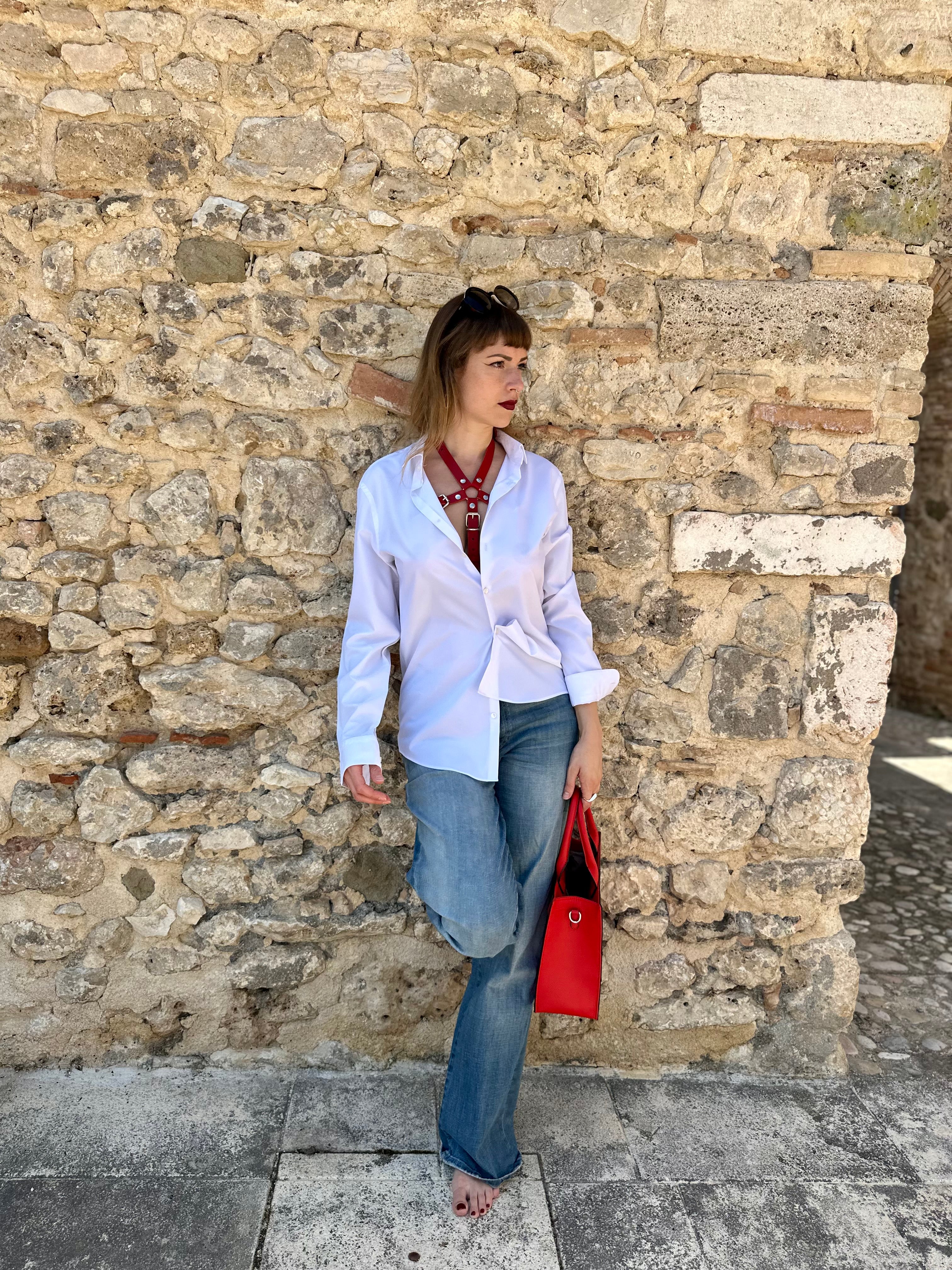 RedTulip Leder Accessoire in Rot  - das Basis Modell, auf der Haut unter einer weißen Bluse, dazu Jeans und eine rote Handtasche. Casual und elegant zugleich. Hier blitzt der obere Teil des  RedTulip  auf. Ganzkörperaufnahme -  XMORENIUM-NERO