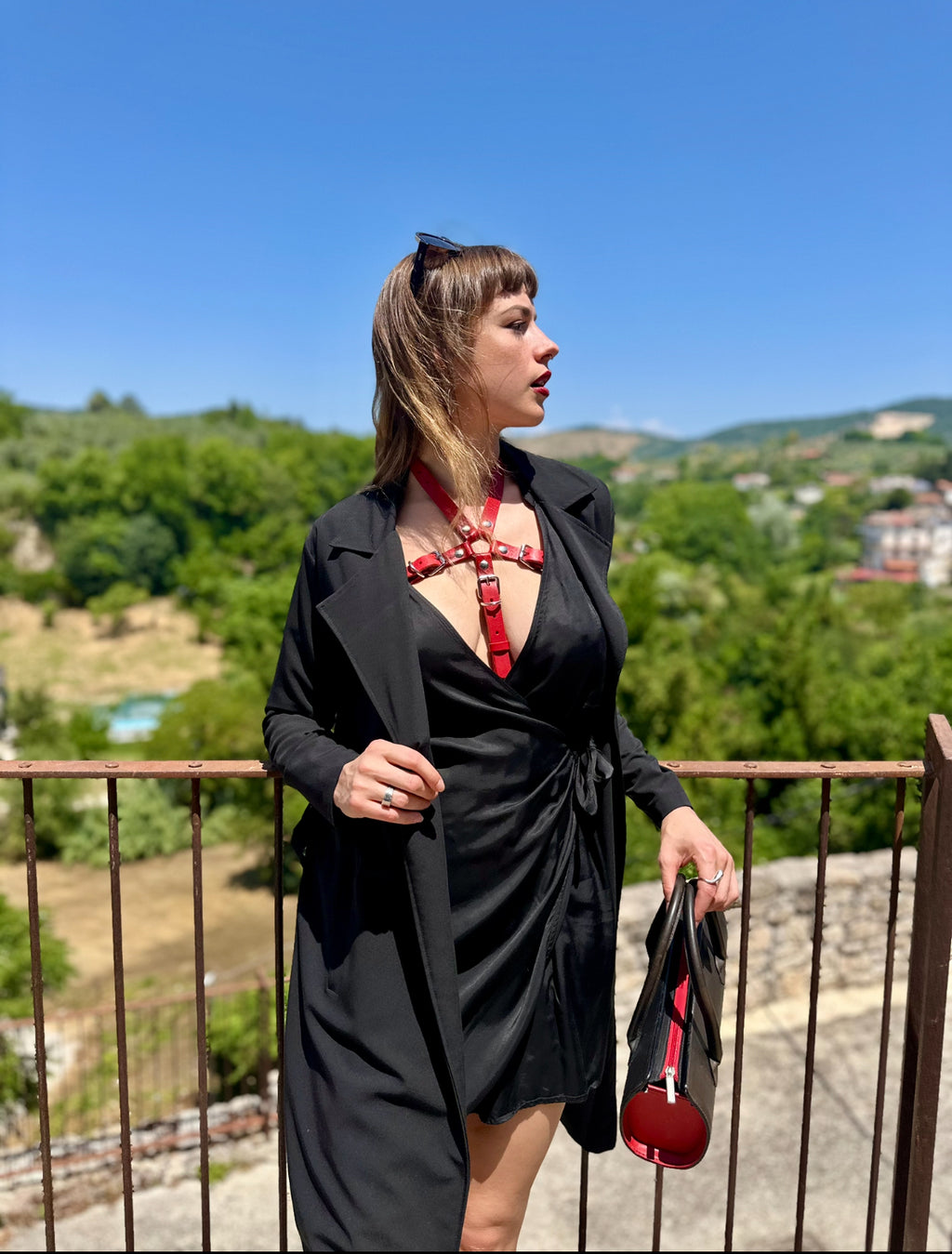 RedTulip Leder Accessoire in Rot - das Basis Modell, auf der Haut unter einem schwarzen Kleid, darüber einen schwarzen Mantel. Hier blitzt der obere Teil des  RedTulip  auf. Ganzkörperaufnahme - XMORENIUM-NERO