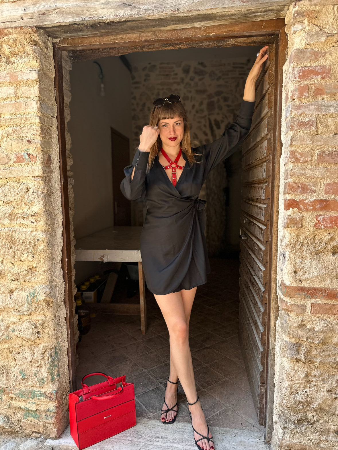 RedTulip Leder Accessoire in Rot  - das Basis Modell, auf der Haut unter einem schwarzen Kleid. Hier blitzt der obere Teil des  RedTulip  auf.  Dazu Absatzschuhe und eine rote Handtasche. Ganzkörperaufnahme - XMORENIUM-NERO