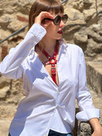 RedTulip Leder Accessoire in Rot  - das Basis Modell, auf der Haut unter einer weißen Bluse, dazu Jeans und eine Sonnenbrille. Casual und elegant zugleich. Hier blitzt der obere Teil des  RedTulip  auf.   - XMORENIUM-NERO